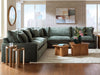 Green sectional sofa in a living room with wooden tables and decor.