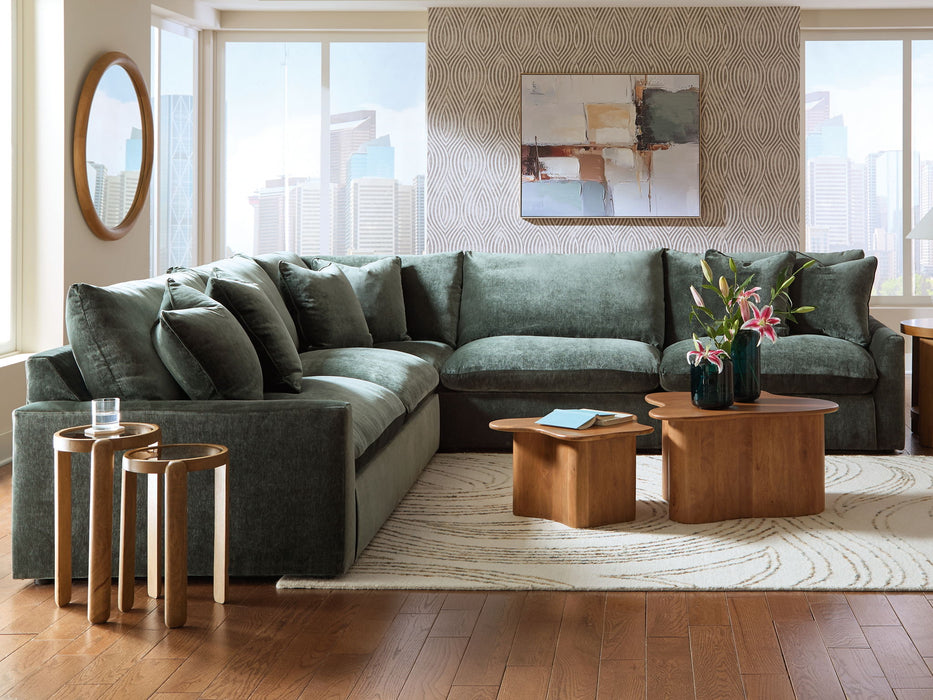 Green sectional sofa in a living room with wooden tables and decor.
